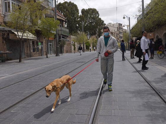 An Israeli wears a mask, for protection against the coronavirus, while walking his dog in Jerusalem, on Tuesday, April 7, 2020.  JER2020040704 DEBBIExHILL
