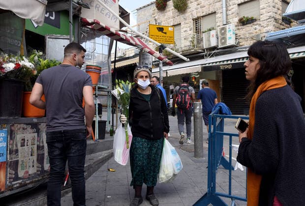 An Israeli woman wears a mask and gloves, as protection from the coronavirus, while shopping for the Jewish holiday Passover in the Mahane Yehuda Market, on Tuesday, March 7, in Jerusalem. Israeli Prime Minister Benjamin announced severe travel restrictions and a curfew for the Passover holiday, as an effort to halt the spread of the coronavirus.  JER2020040708 DEBBIExHILL