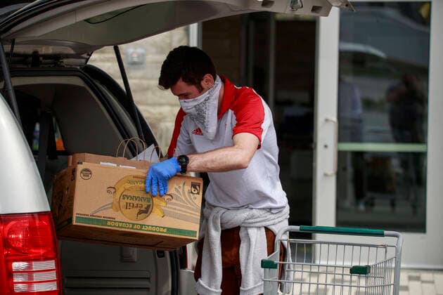 April 11, 2020, Bloomington, Indiana, United States: A man wearing a face mask and gloves and working for the Bloomington Community Farmers Marketm, carries an order to a customer as food is being distributed in a drive-thru arrangement at the Switchyard Pavilion. Bloomington United States - ZUMAs197 20200411_zaa_s197_172 Copyright: xJeremyxHoganx