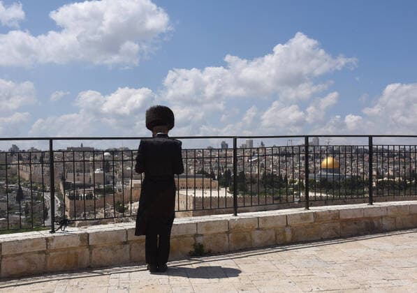 An Ultra-Orthodox Jew prays on the Mt. of Olives, overlooking the Old City of Jerusalem, on Sunday, April 12, 2020. The Israeli government deployed a 1,000 police to enforce a full closure on Jewish religious neighborhoods with the highest rate of coronavirus in Jerusalem. According to the Health Ministry about 75 percent of the infected in Jerusalem live in the Ultra-Orthodox neighborhoods.  JER2020041205 DEBBIExHILL
