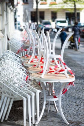 Corona Life The white tables and chairs are piling up, tied up with red and white flutterband, in front of a restaurant in Mommsenstrasse, Berlin Charlottenburg Corona Coronavirus Shutdown Restrictions Dealing with Corona Corona Everyday life Restaurants OPEN FOR TAKE AWAY Take away Tables and chairs are piling up Tables and chairs Chairs Flutterband Berlin Berlin Deu
