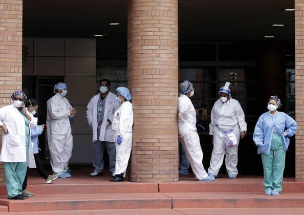 Healthcare workers wearing protective face masks and medical clothes stand outside of an entrance to Wyckoff Heights Medical Center in New York City on Tuesday, April 14, 2020. As of today nearly 285,000 have been infected with Coronavirus and more than 14,000 people have died in NY, NJ and CT. There are signs however that the curve is flattening.  NYP20200414119 JOHNxANGELILLO