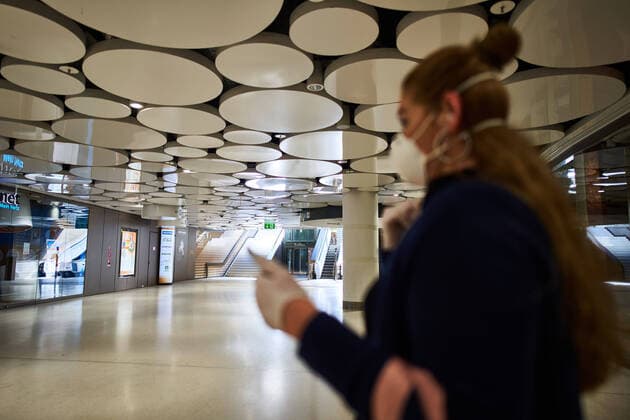 Munich, Germany, April 15, 2020. A woman with mouth protection and mobile phone at empty underground Stachus place with shopping areas due to the Corona virus disease (COVID-19) on April 15, 2020 in Munich, Germany.