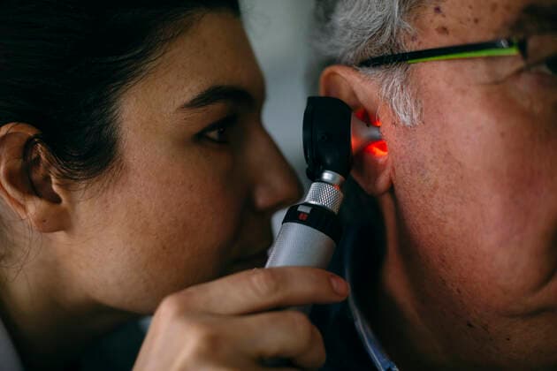 ENT physician examining ear of a senior man with an otoscope model released Symbolfoto property released ABZF03031