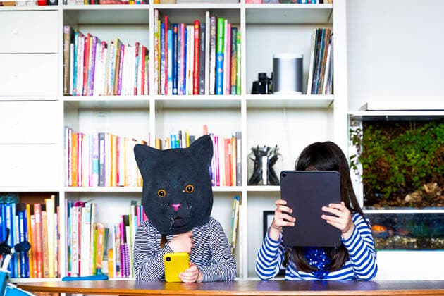 Two girls sitting at table, hiding behind digital tablet and cat mask model released Symbolfoto property released ERRF03439