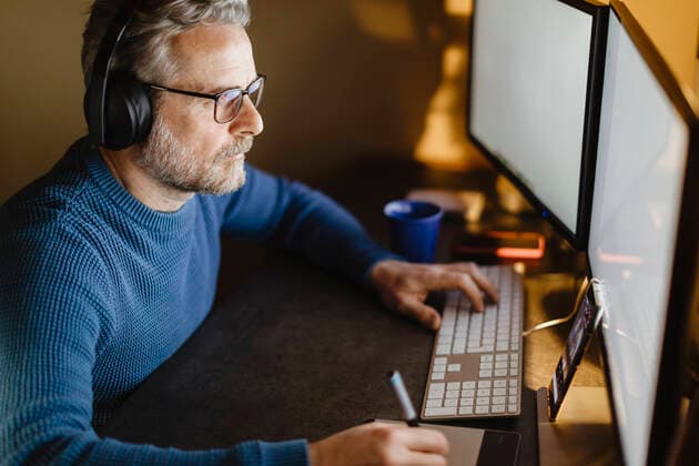 Mature man with headphones sitting at desk at home working with graphics tablet and computer model released Symbolfoto property released MCVF00300