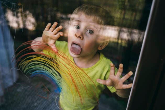 Portrait of little boy standing behind balcony door licking glass pane with drawn rainbow model released Symbolfoto property released MFF05419