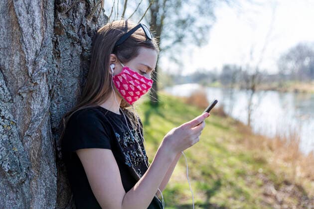 Girl with homemade protective mask using smartphone and leaning on tree model released Symbolfoto SARF04536