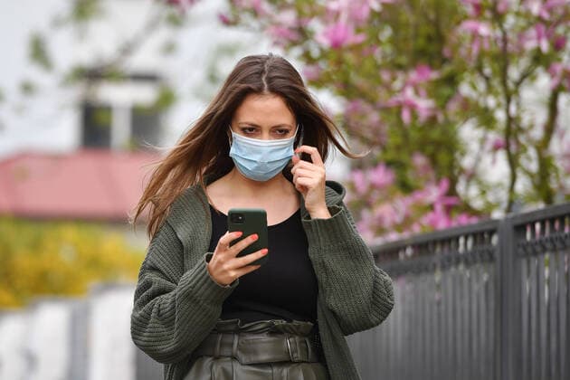 Theme picture Corona A young woman with protective mask, mouth guard, community mask looks at her smartphone on 24 04 2020