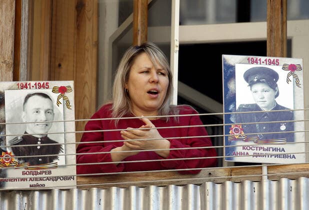 ROSTOV-ON-DON, RUSSIA - APRIL 25, 2020: A local woman shows portraits of her relatives who fought in the 1941-1945 Great Patriotic War, as she listens to singers of the Song and Dance Ensemble of the Russian Army Southern Military District perform outside a block of flats to cheer up people who have to stay at home due to lockdown measures amid the pandemic of the novel coronavirus disease (COVID-19). The open-air concert is part of a series of concerts, which the military musicians plan to perform in various residential areas of the city ahead of the forthcoming 75th anniversary of Soviet Victory in the Great Patriotic War (part of WWII). Rostov-on-Don has been on lockdown since 31 March 2020. Valery Matytsin TASS  TS0D70B7