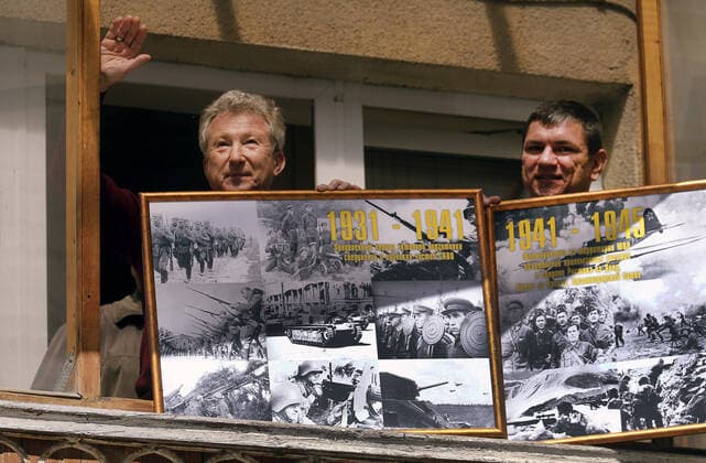 ROSTOV-ON-DON, RUSSIA - APRIL 25, 2020: Local men on a balcony show photographs of Red Army trooops taken shortly before and during the 1941-1945 Great Patriotic War, as they listen to singers of the Song and Dance Ensemble of the Russian Army Southern Military District perform outside a block of flats during the pandemic of the novel coronavirus disease (COVID-19). The open-air concert is part of a series of concerts, which the military musicians plan to perform in various residential areas of the city ahead of the forthcoming 75th anniversary of Soviet Victory in the Great Patriotic War (part of WWII). Rostov-on-Don has been on lockdown since 31 March 2020. Valery Matytsin TASS  TS0D70B8