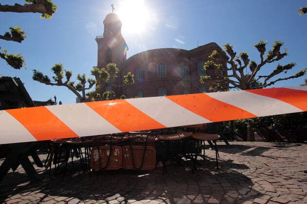 Barrier tape in front of stacked tables and chairs of a closed café s on Paulsplatz in front of the Paulskirche in the most beautiful sunshine in downtown Frankfurt, Hesse, Germany