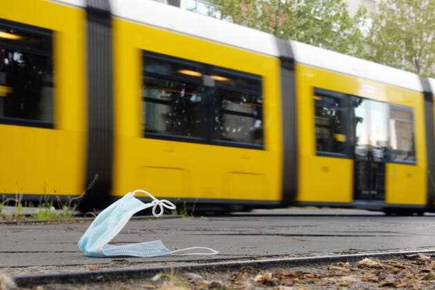 03 05 2020, Berlin Germany A breathing mask lies lost or thrown away on the sidewalk, a tram reminds of the mask obligation in public transport, at the BVG
