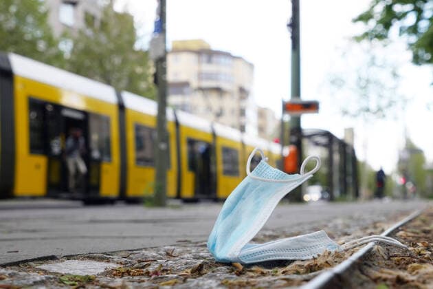 03 05 2020, Berlin Germany A breathing mask lies lost or thrown away on the sidewalk, a tram reminds of the mask obligation in public transport, at the BVG