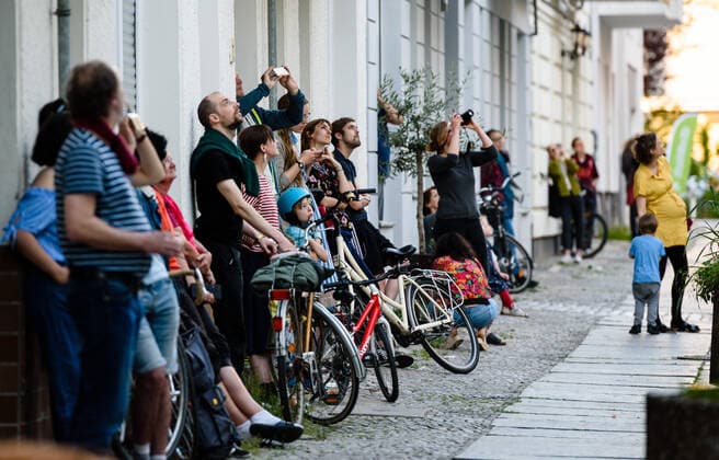 May 9, 2020, Berlin, Berlin, Germany: Several people gather on the sidewalk while the musician Junk-E-cat gives a spontaneous concert on the roof of a house. The Berlin-based musician Junk-E-cat combines acoustic and electronic elements and seamlessly combines a selection of reed instruments with finger drumming and live looping. Since 4 May, open-air meetings with up to 50 participants are generally permit-free, provided that distance and hygiene rules are observed. Berlin Germany - ZUMAs172 20200509_zap_s172_003 Copyright: xJanxScheunertx