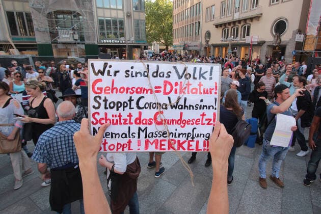 An authorized demonstration against the corona infection protection law and the associated restrictions on freedom took place in the city center of Cologne, North Rhine-Westphalia, Germany A demonstrator holds a poster with the words we are the people, obedience equals dictatorship, stop Corona madness, protect the constitution, niemas mass vaccinations, stop Merkel