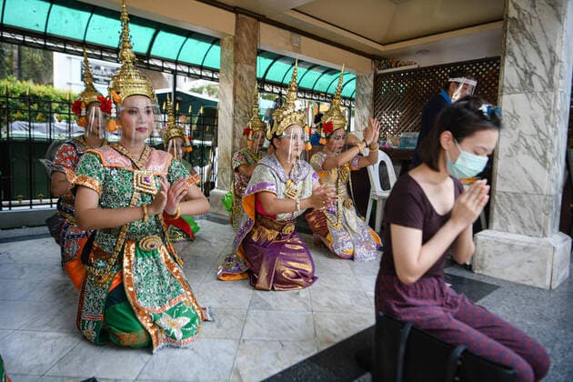May 5, 2020, Bangkok, Thailand: Traditional Dancers at the Erawan shrine, a popular tourist™s site perform while wearing face shields next to a woman offering prayers, wearing a face mask as a precaution following the government ease of some coronavirus restrictions during lockdown. Bangkok Thailand - ZUMAs197 20200505_zab_s197_145 Copyright: xAmpholxThongmueangluangx