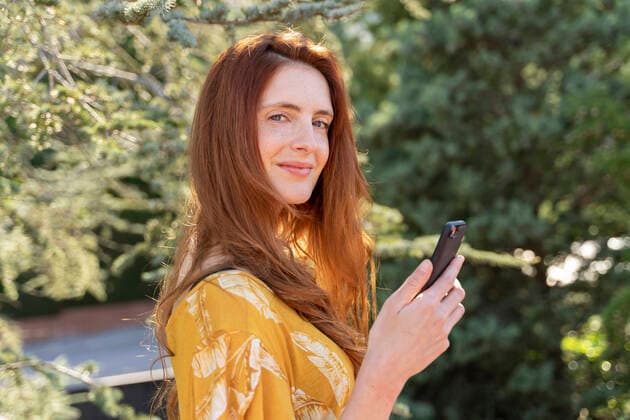 Portrait of smiling redheaded woman with smartphone outdoors model released Symbolfoto AFVF06191
