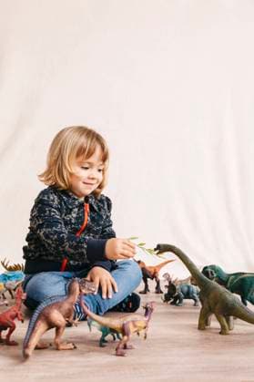 Portrait of cute little girl sitting on the floor feeding toy dinosaur model released Symbolfoto JRFF04411