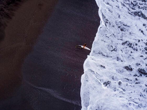 Indonesia, Bali, Pererenan Beach, Aerial view of lone surfer at black coastal beach KNTF04532