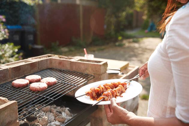 Midsection of woman holding plate with skewers while standing by barbecue grill at back yard on sunny day model released Symbolfoto property released PMF01045
