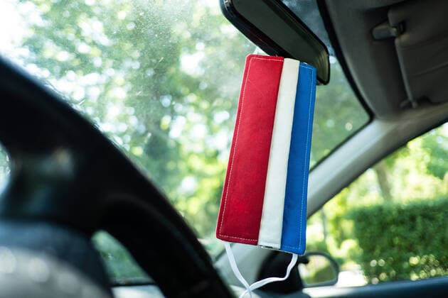 A self-sewn respirator mask with the colors of the Dutch flag hangs in the car on a rear view mirror düsseldorf North Rhine-Westphalia Germany
