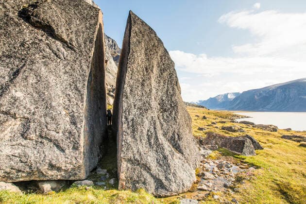 Backpacker squeezes through cracked erratic rock in the arctic. Pangnirtung, NU, Canada CR_JDIP200331-320724-01,model released, Symbolfoto