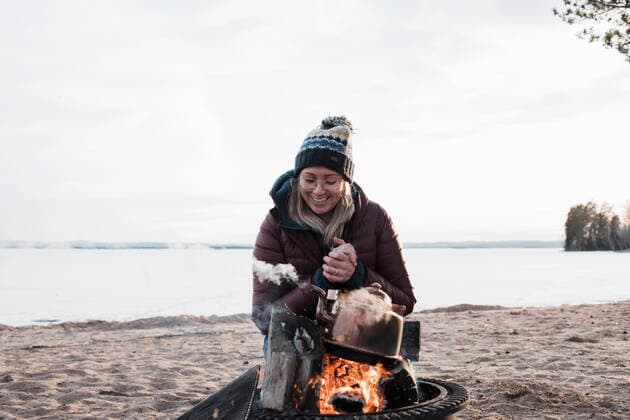 woman smiling warming up by a camp fire on the beach in winter Bjuraker, Gavleborg County, Sweden CR_RABE200331-336446-01,model released, Symbolfoto