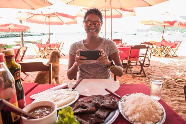woman at beach restaurant taking picture of food Angra dos Reis, RJ, Brazil CR_THHE200430-370692-01,model released, Symbolfoto
