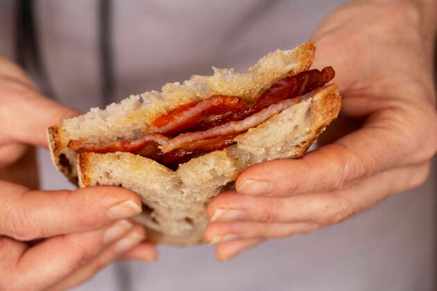 Close up of person holding bacon sandwich with tomato sauce. Coffee Shop,United Kingdom,Close up of person holding bacon sandwich with tomato sauce.  Close up of person holding bacon sandwich with tomato sauce.