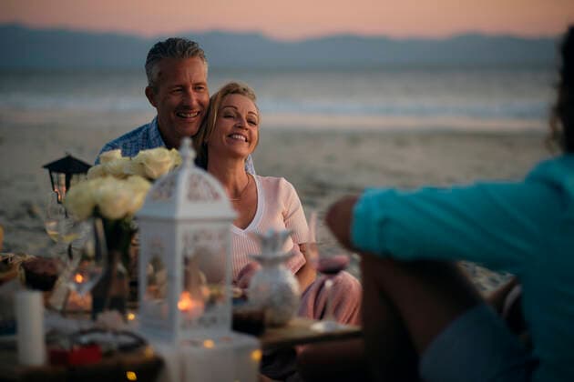 Smiling mature couple looking at male friend while enjoying sunset dinner party at beach, Riviera Nayarit, Mexico. model released Symbolfoto ABAF02302