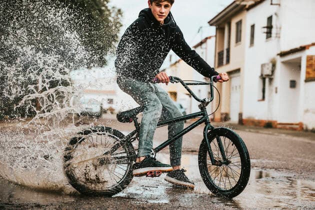 Creative Highlights Symbolfotos Confident teenage boy splashing water in puddle while cycling on street during rainy season model released Symbolfoto ACPF00722
