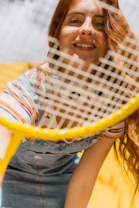 Happy young woman looking through badminton racket during sunny day model released Symbolfoto property released AFVF06442