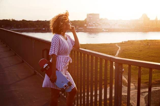 Woman with skateboard enjoying view from bridge during sunset model released Symbolfoto MJFKF00357