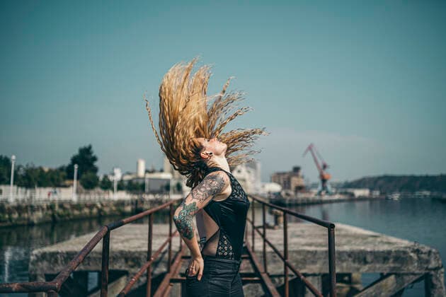 Side view of young tattooed woman tossing her long blond hair while standing hands in pockets on pier during sunny day model released Symbolfoto property released MTBF00390
