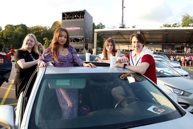 MOSCOW, RUSSIA - JULY 4, 2020: Young people pose for a photograph at a drive-in concert by The Hatters gypsy folk rock band in Luzhniki. The concert, in which the sound is broadcast to the cars via FM radio, is part of LIVE&DRIVE, a series of live drive-in concerts organised by the TCI concert agency and SAV Entertainment Group during the pandemic of the novel coronavirus disease (COVID-19). Vyacheslav Prokofyev TASS  TS0DF272