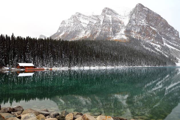 The small wooden canoe rental cabin on Lake Louise s shores, framed by the evergreens and snow-capped Rocky Mountains each reflected in the lake s tranquil waters on a foggy morning in Alberta, Canada. Lake Louise Alberta Canada Copyright: xChuckxDavidx xVWPicsx CHD043A8812Lake Louise