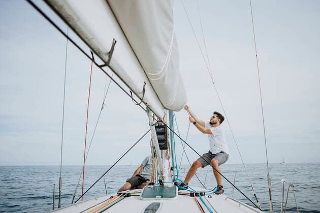 Sailor maneuvering setting the mainsail in sailboat against sky model released Symbolfoto property released GMLF00303