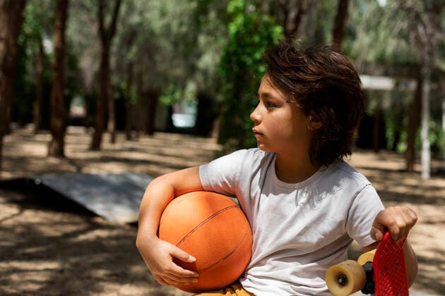 IMAGO Creative: Lokalhelden - Jugendsportbildung Thoughtful boy with basketball and skateboard in park model released Symbolfoto VABF02979
