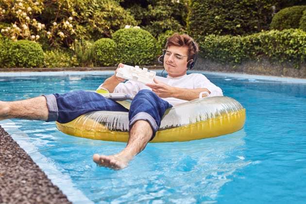 Young man working from home office on airbed in swimming pool looking at architectural model model released Symbolfoto property released UKOF00003