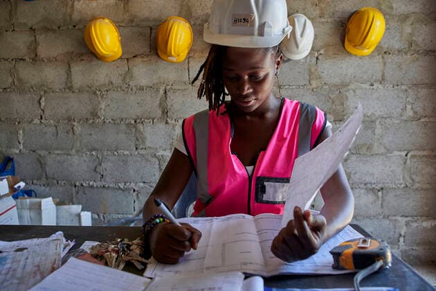 Female building contractor analyzing blueprint on desk while sitting in school model released Symbolfoto property released VEGF02503