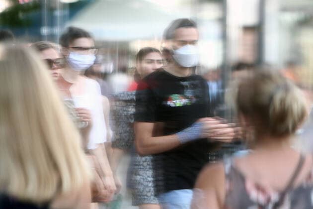 Passers-by with and without mouth and nose cover are reflected in a shop window pane in the shopping street and pedestrian zone Neuhauser Straße Kaufingerstraße in downtown Munich, Bavaria, Germany