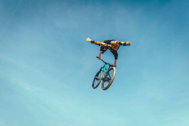 Young man performing stunt with bicycle against blue sky at park during sunset model released Symbolfoto ACPF00782