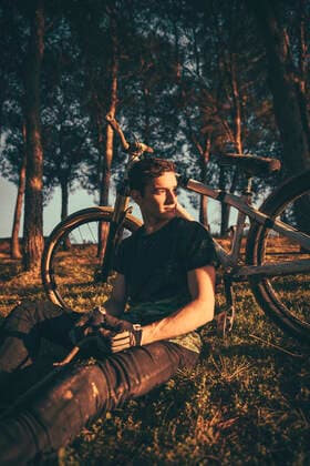 Thoughtful young man sitting by bicycle in park during sunset model released Symbolfoto ACPF00785