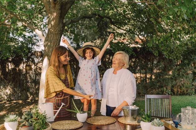 Cheerful girl with arms raised standing with mother and grandmother against tree in yard model released Symbolfoto property released ERRF04173