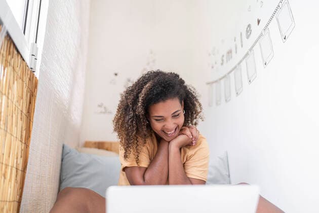 Creative Highlights Symbolbilder Cheerful woman with curly hair video conferencing over laptop while sitting by wall at home model released Symbolfoto property released SNF00529