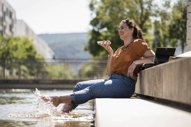 IMAGO Creative: Sommer, Sommertage im Stadtpark Cheerful woman with legs in pond talking over smart phone while sitting at park model released Symbolfoto UUF20794