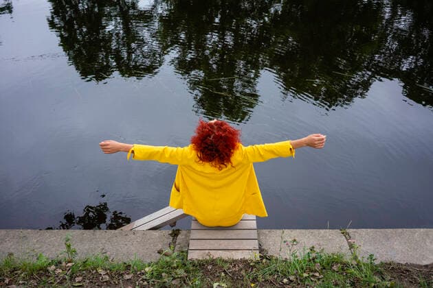 Young woman with curly hair and yellow suit sitting by the riverside with arms outstretched model released Symbolfoto VPIF02818
