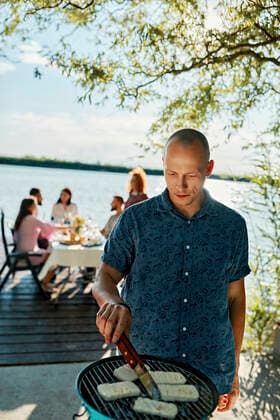 Man grilling Halloumi cheese at a lake with friends in background model released Symbolfoto ZEDF03564