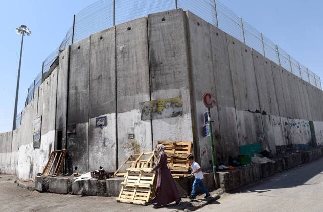 Palestinians walk beside the Israeli separation wall around the Shurafat Refugee Camp near Jerusalem, on Monday, August 31, 2020. Senior U.S. Presidential Advisor Jared Kushner called on Palestinians to return to the negotiations with Israel and not be stuck in the past upon arrival to the AUE on the first direct flight from Israel to Abu Dhabi.  JER2020083110 DEBBIExHILL